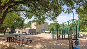 Ein Park mit Picknicktischen, einem Spielplatz und einem Gebäude im Hintergrund.