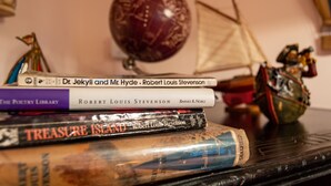 Une pile de livres, dont les titres sont « Le docteur Jekyll et M. Hyde » et « L’île au trésor », est posée sur une table.
