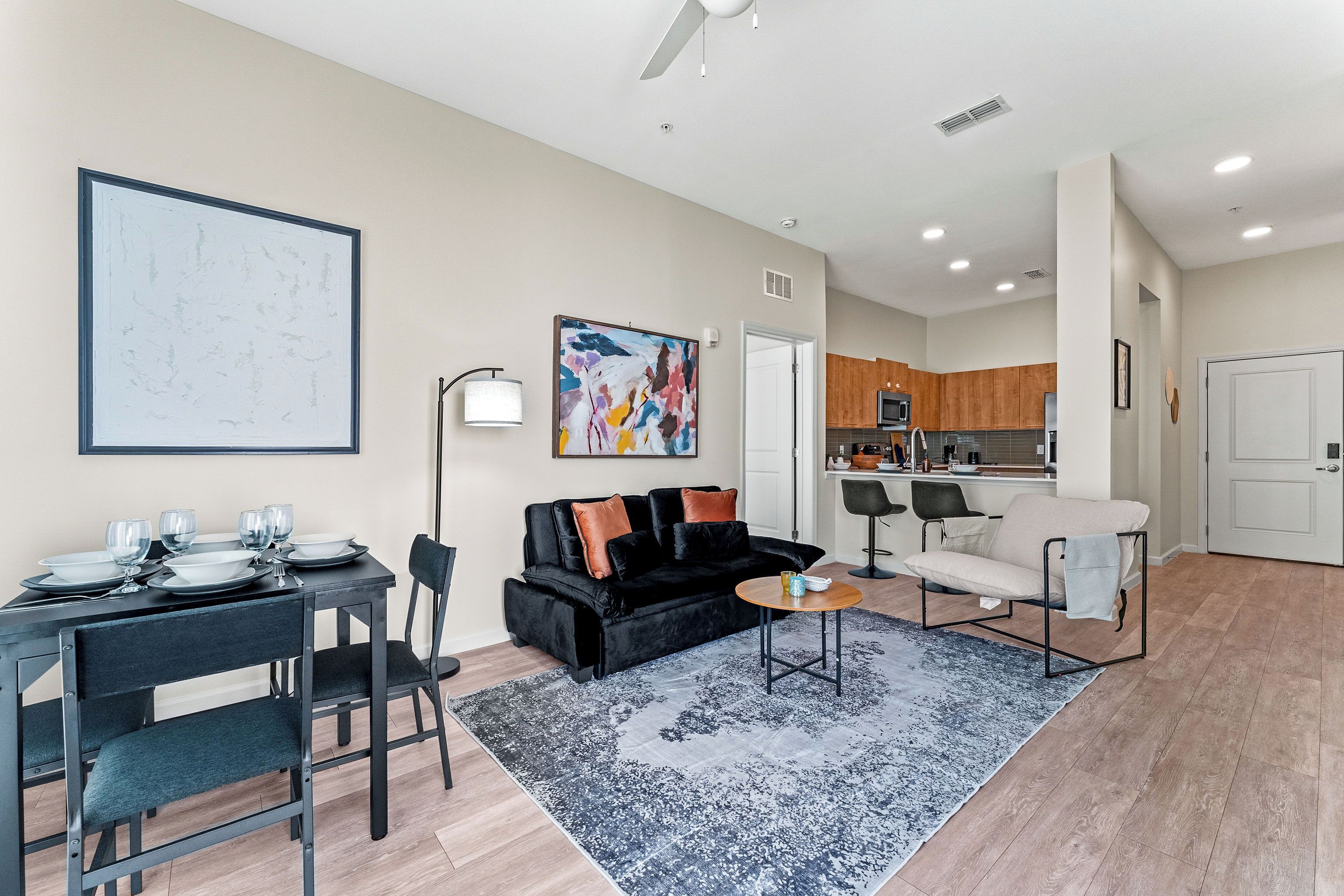 Un apartamento moderno con comedor, un sofá negro, cocina y sala de estar.