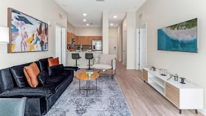 A modern living room with a black leather sofa, a round coffee table, and a minimalist white console table. - Riviere 2BR Apartment Pet Friendly Oasis Sleeps 6 Close to Epic Universe Pool & Gym (Orlando)