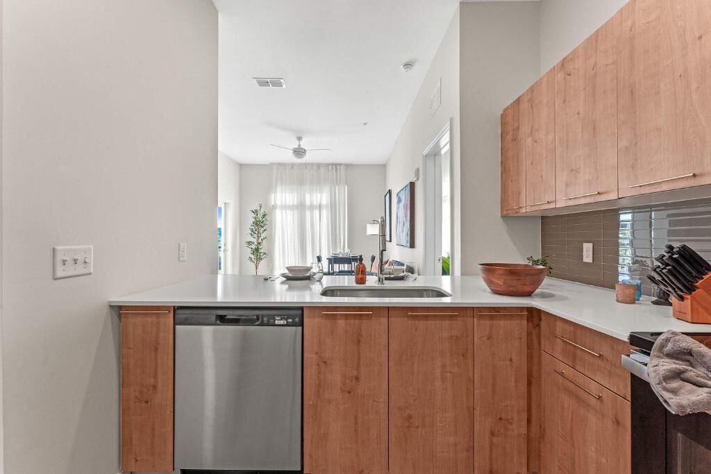 A modern kitchen with wooden cabinets, a stainless steel dishwasher, and a countertop with various kitchen items.