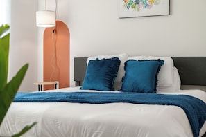 Un letto rifatto con una coperta blu, una testiera grigia e un tavolino rotondo vicino.