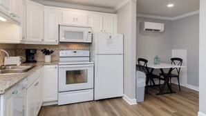 Een keuken met witte kasten, een magnetron, een koelkast, een fornuis en een eethoek met een tafel en stoelen.