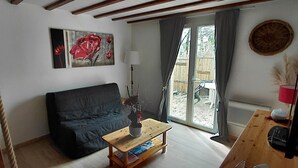 Un salon avec un canapé foncé, une table basse en bois, un tableau, une lampe et une vue à travers une porte vitrée.