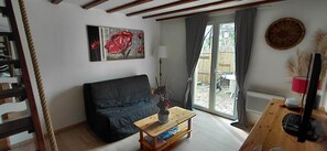 A living room with a dark sofa, a wooden coffee table, a painting, a lamp, and a view through a glass door. - Cocoon in quiet residence with private garden (Malissard)