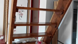 Un escalier en bois avec une corde, une commode en bois et un réfrigérateur à l’arrière-plan.