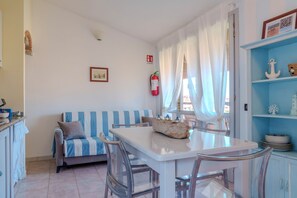 A dining area with a white table, clear chairs, a blue-striped sofa, and a blue cabinet with decorative items.