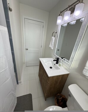 Une salle de bain avec un lavabo blanc, un meuble-lavabo en bois, un grand miroir et des toilettes blanches.