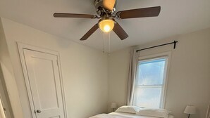 Ein Schlafzimmer mit einem Bett, einem Deckenventilator, einem Fenster mit Jalousien und einem Teppich.