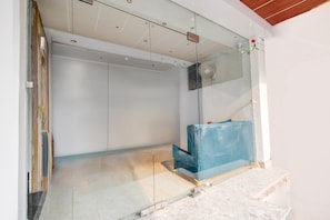 A room with a glass partition, a blue protective cover on a piece of furniture, and a ceiling with recessed lighting.