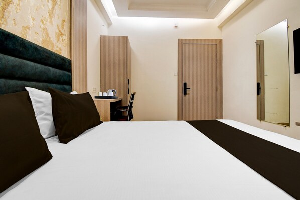 A hotel room with a bed, a bedside table with a lamp, a chair, and a door.