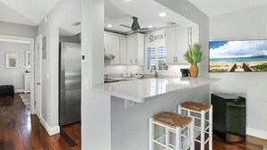 A modern kitchen with white cabinetry, a stainless steel refrigerator, and a large island with bar stools. - Delray Breezes !NEW! WALK to BEACH & THE AVE! (Delray Beach)