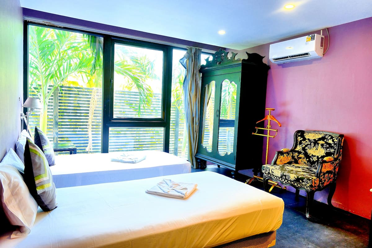 A hotel room with two beds, a wardrobe, a chair, and an air conditioning unit.