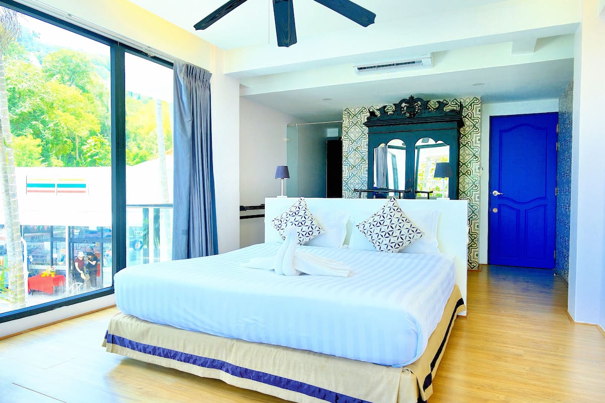A hotel room with a large bed, a view through a sliding door, a blue door, and a mirror with a decorative frame.