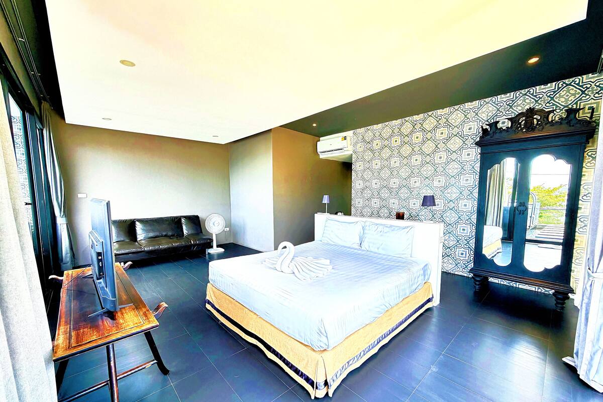A bedroom with a bed, a TV, a sofa, a cabinet, and a desk.