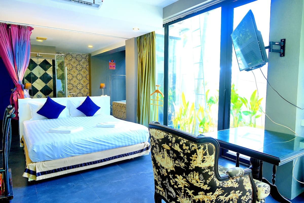 A hotel room with a bed, a desk, a chair, a TV, and a large window.