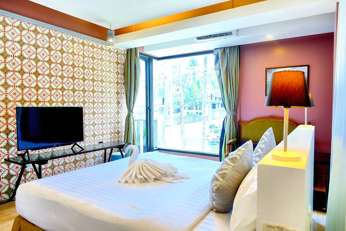 A hotel room with a bed, a TV, a window with curtains, and a lamp.