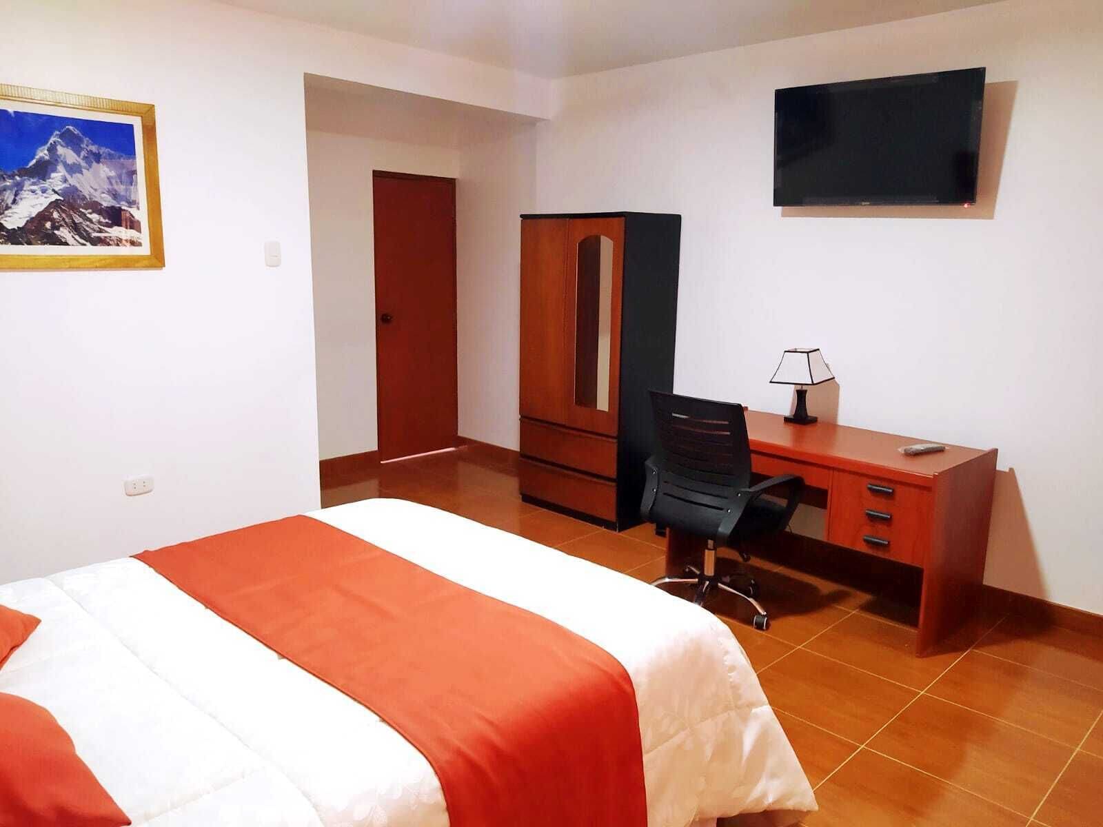 A hotel room with a bed, a desk, a chair, a wardrobe, a television, and a framed picture on the wall.