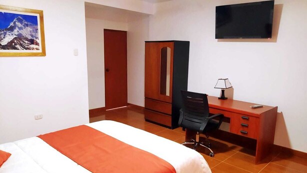 Habitación de hotel con cama, escritorio, silla, armario, televisor y un cuadro en la pared.