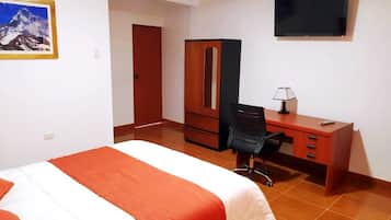Habitación de hotel con cama, escritorio, silla, armario, televisor y un cuadro en la pared.