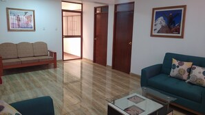 A living room with a sofa, a coffee table, and a blue armchair. There are two doors and a window. - CASA TALIOS (Carhuaz)