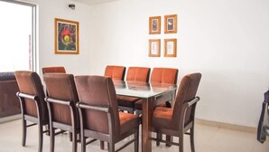A dining area with a glass-top table surrounded by six chairs, a white wall with framed pictures, and a door to the left. - CASA TALIOS (Carhuaz)