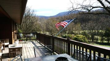 A wooden deck with outdoor seating, a flag, and a view of a forested area.
