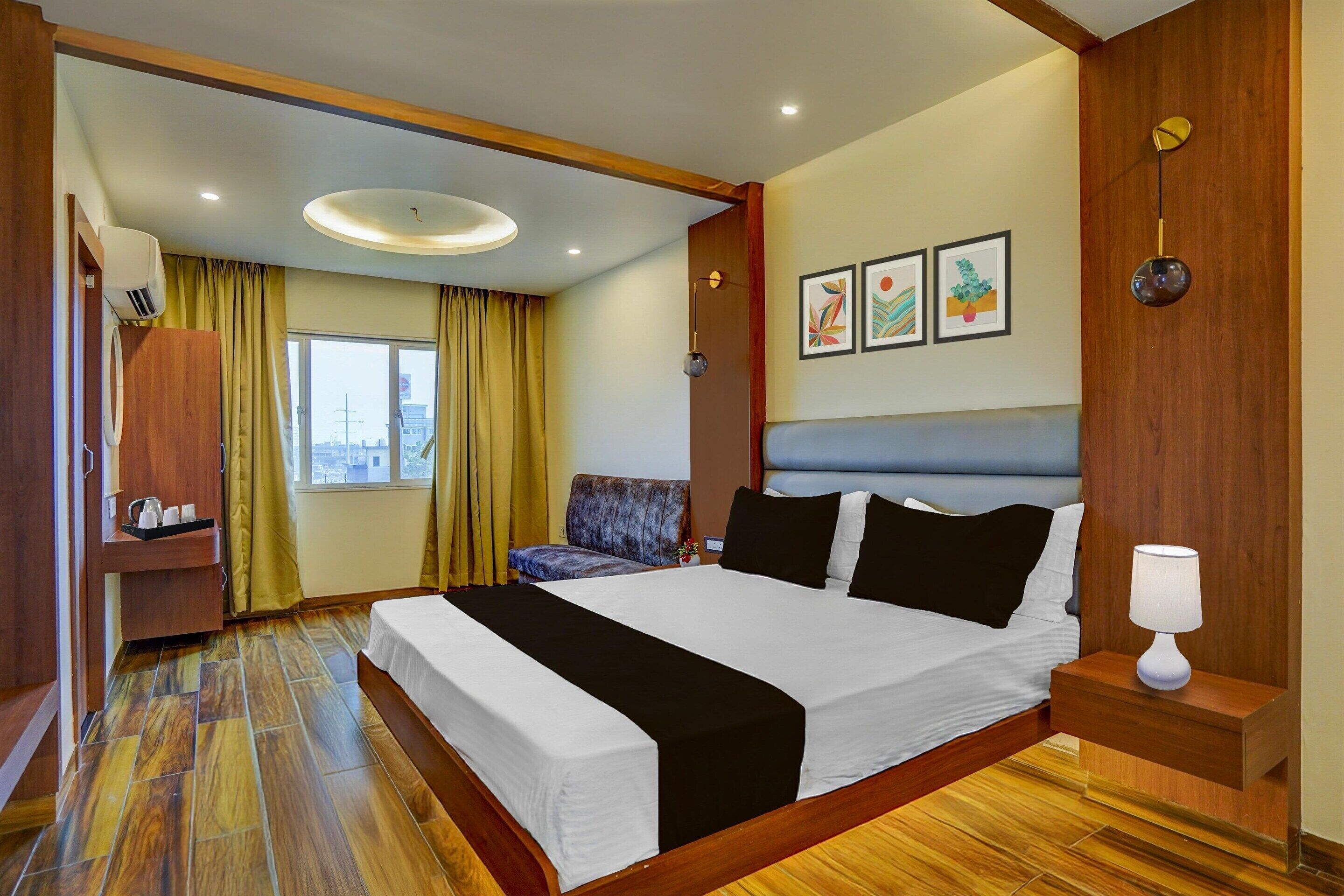 Een hotelkamer met een groot bed, een nachtkastje met een lamp, een bureau met een stoel, en een raam met gordijnen.