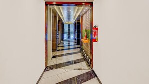A hotel corridor with a checkered floor, glass doors, a fire extinguisher, and a brick wall. - Deluxeclassic Court (Patna)