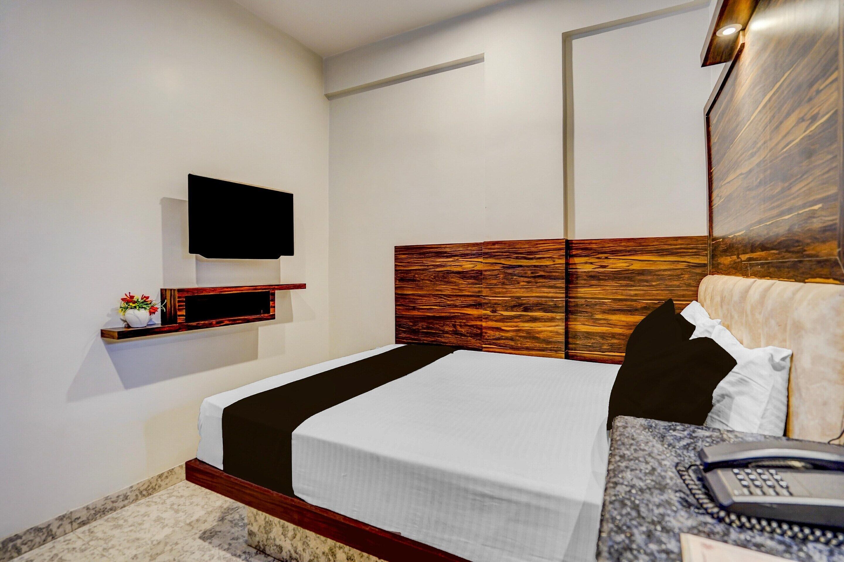 Ein modernes Hotelzimmer mit einem Holzkopfende, einem flachbildfernseher an der Wand, einem Nachttisch mit Telefon und einer kleinen Ablage mit einer Vase.