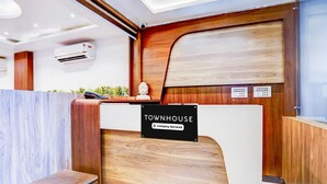 A reception desk with a sign reading 'TOWNHOUSE Company-Serviced,' a wooden panel wall, a Buddha statue, and an air conditioning unit. - Deluxeclassic Court (Patna)