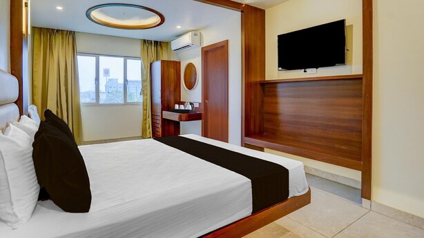 A hotel room with a bed, a TV mounted on the wall, a window with curtains, and an air conditioning unit. - Deluxeclassic Court (Patna)