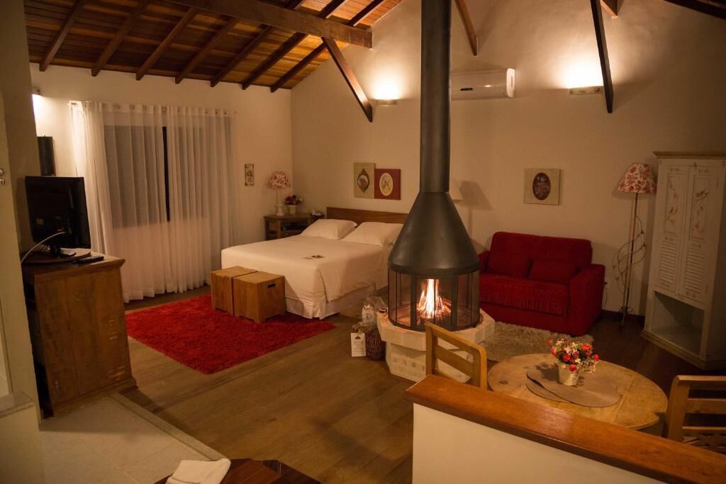 A cozy room with a bed, a red sofa, a table with a vase, and a fireplace.