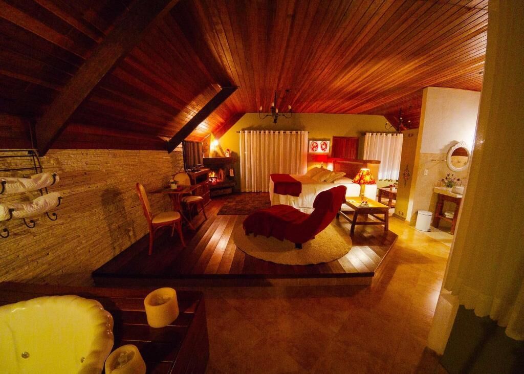 Ein Dachzimmer mit Holzbalken, einem roten Sessel, einem kleinen Tisch und einem Bett mit Vorhängen.