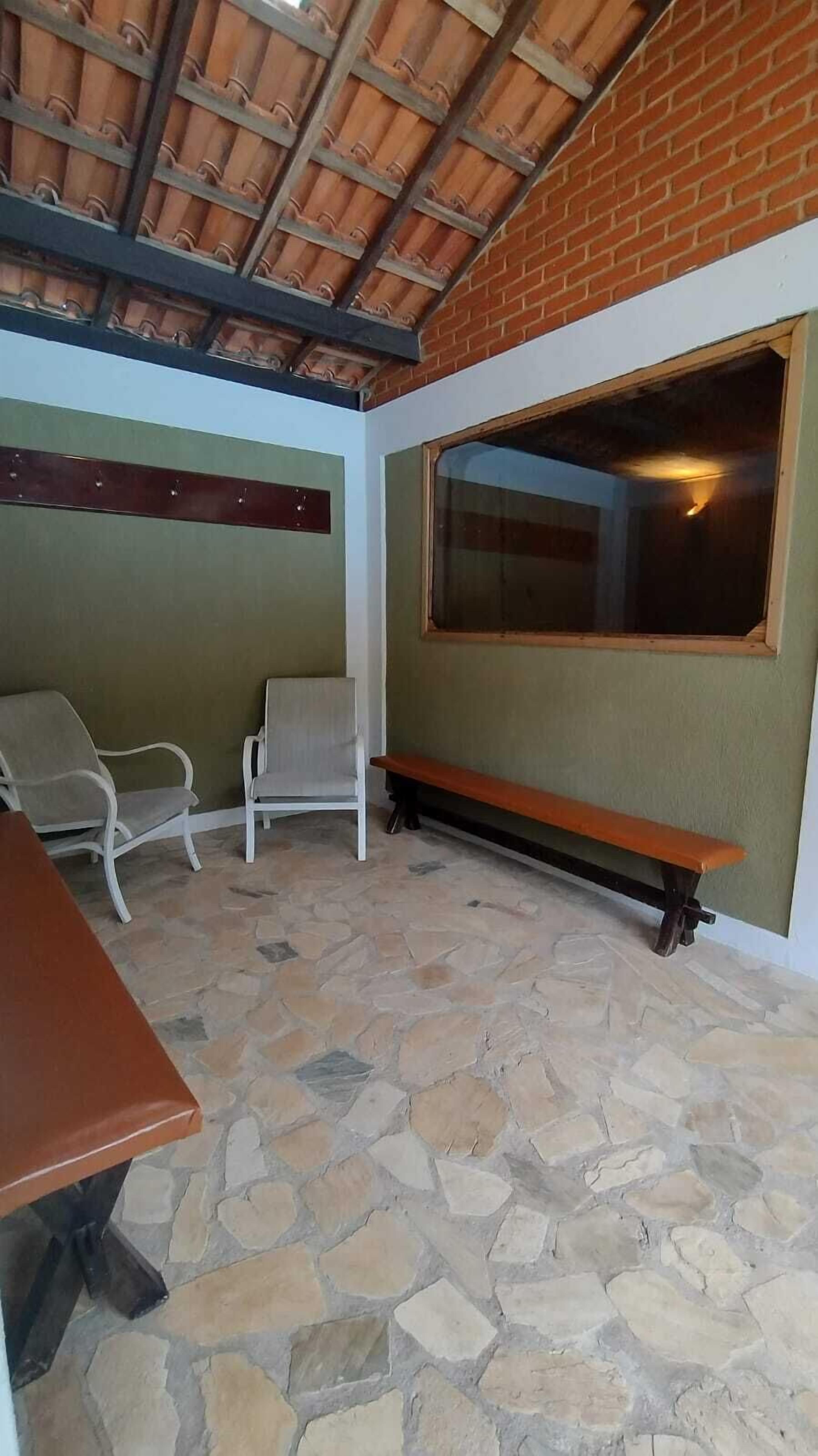 A covered patio area with stone flooring, a bench, two chairs, and a table.