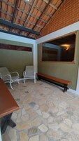 A covered patio area with stone flooring, a bench, two chairs, and a table.