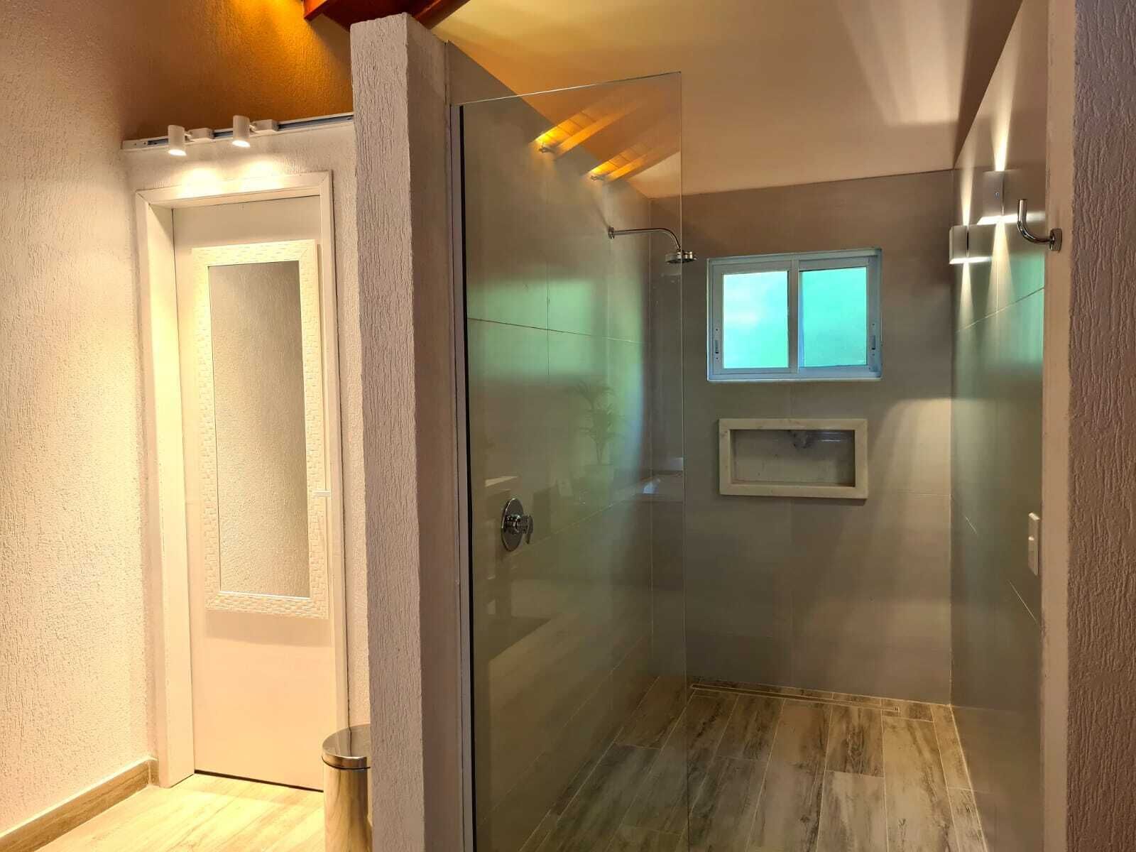 A modern bathroom with a glass shower enclosure, a small window, and a wooden floor.