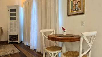 A room with a round wooden table, two white chairs with woven seats, a white cabinet, and a framed picture on the wall.