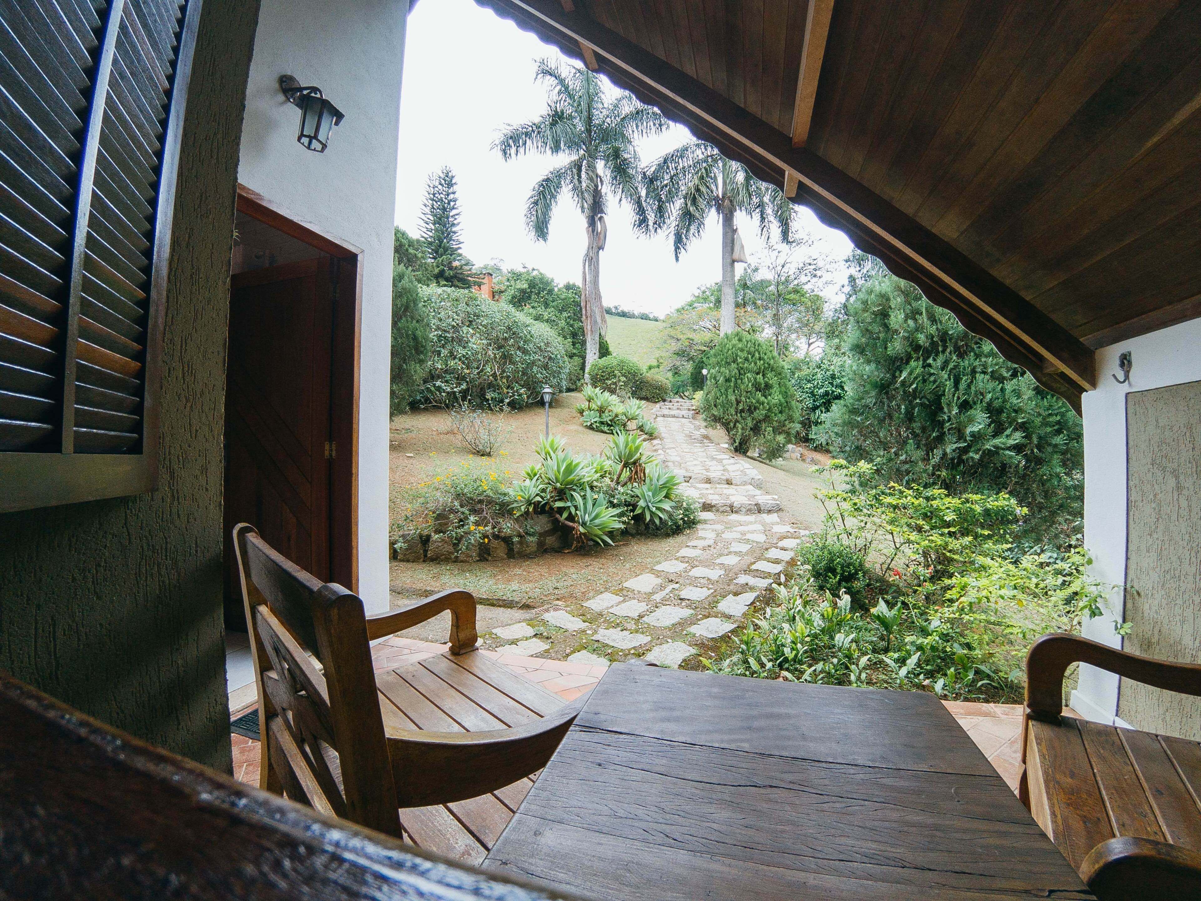 An open wooden door leading to a garden with a stone path, benches, and a lamp post.