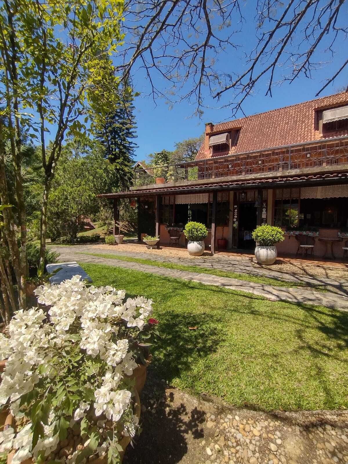 Un edificio tradicional con tejado de baldosas, porche cubierto y un jardín bien cuidado con flores blancas.