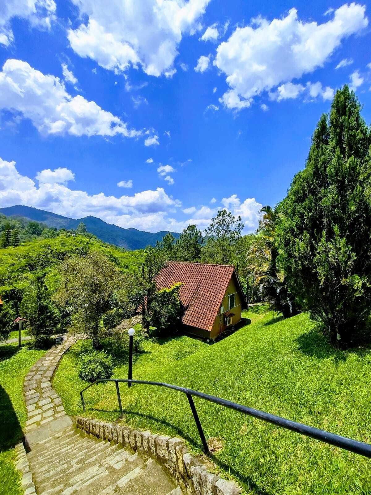 Une maison avec un toit rouge, entourée d’une végétation luxuriante et sous un ciel bleu clair.