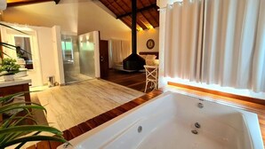 Una habitación amplia con una bañera grande, piso de madera y un techo alto con vigas a la vista.