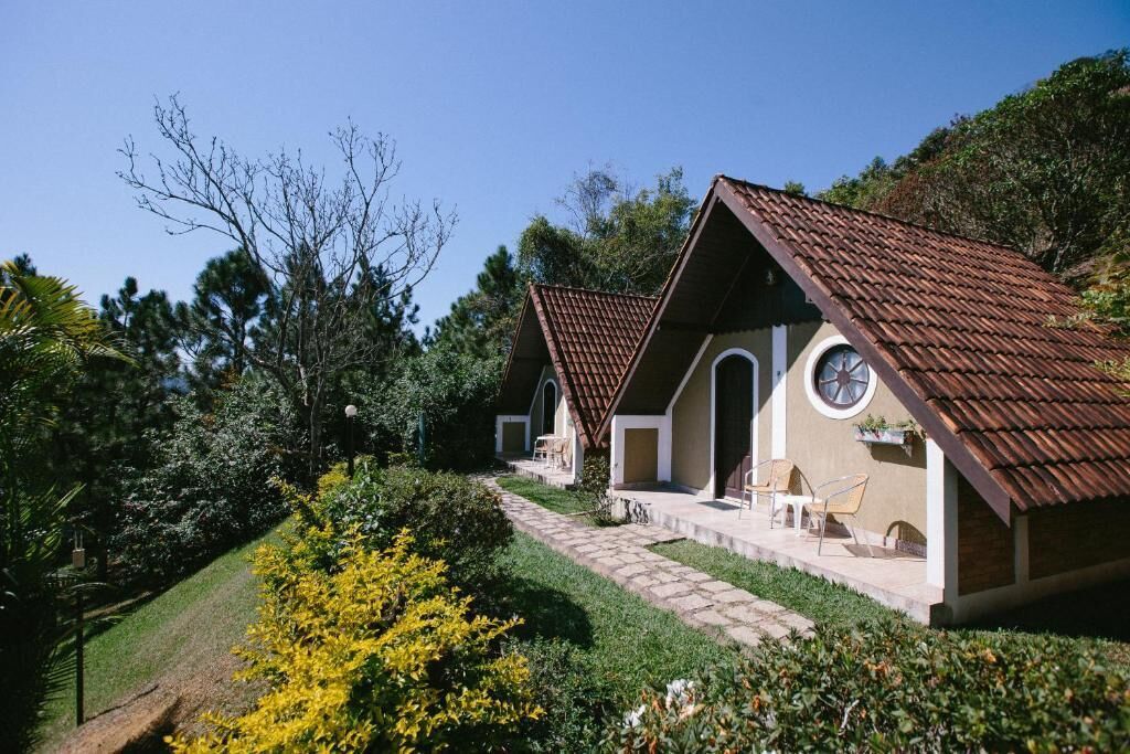 Uma fileira de pequenas casas térreas com telhados inclinados, um caminho pavimentado e um jardim com flores amarelas.