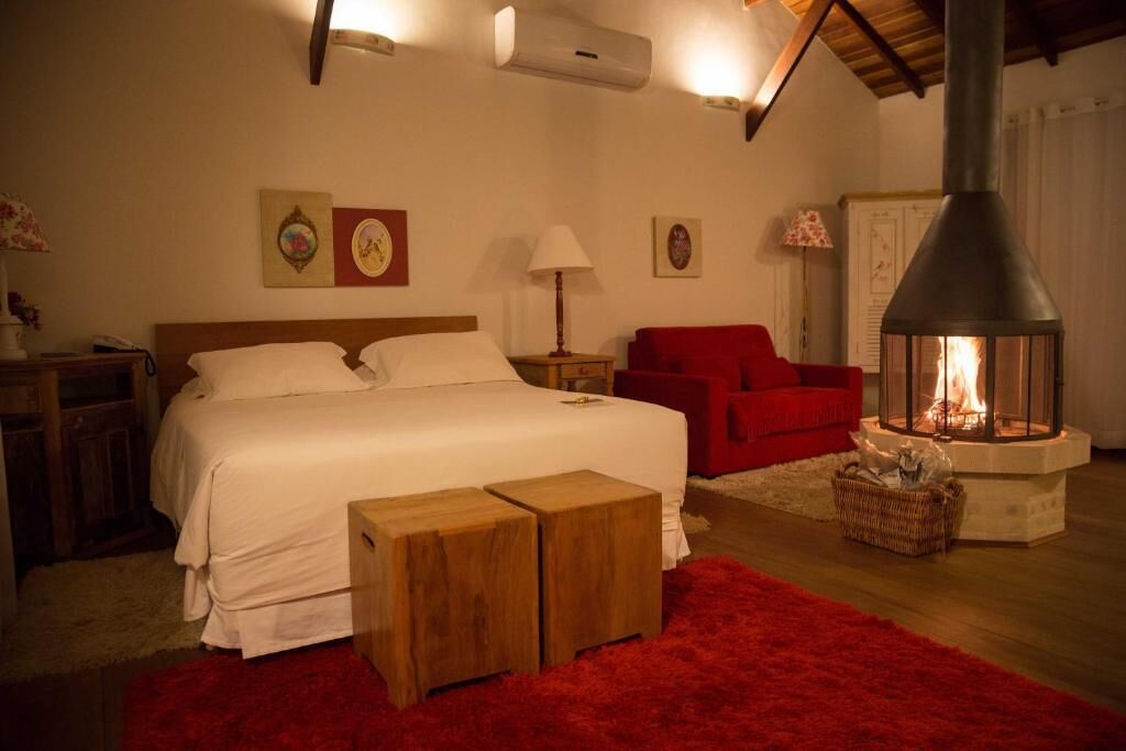 Un dormitorio con cama, un sillón rojo, chimenea y un banco de madera.