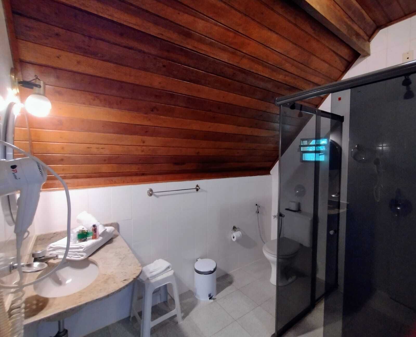 Een badkamer met een houten plafond, een glazen douchecabine, een witte wastafel en een spiegel.