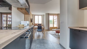 Una cocina moderna con encimera de madera, comedor con mesa y sillas, y vistas a través de amplios ventanales.