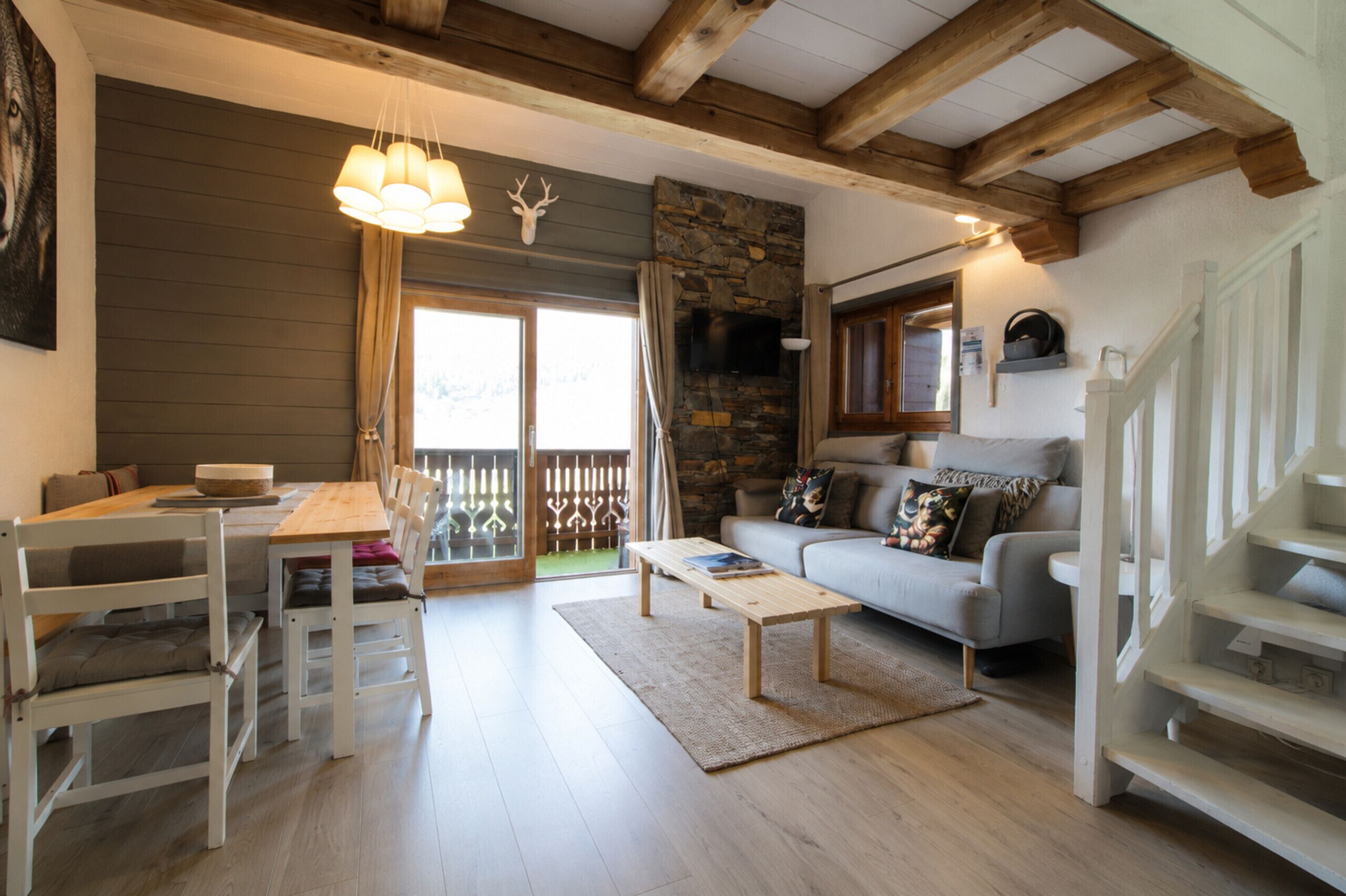 Ein gemütliches Wohnzimmer mit Kamin aus Stein, einem Essbereich mit Holztisch und -stühlen, einem grauen Sofa und einer Treppe.
