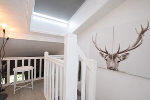 A staircase with white railings, a white wall with a deer head painting, and a small white table. - Apartment Barberine (Les Houches)