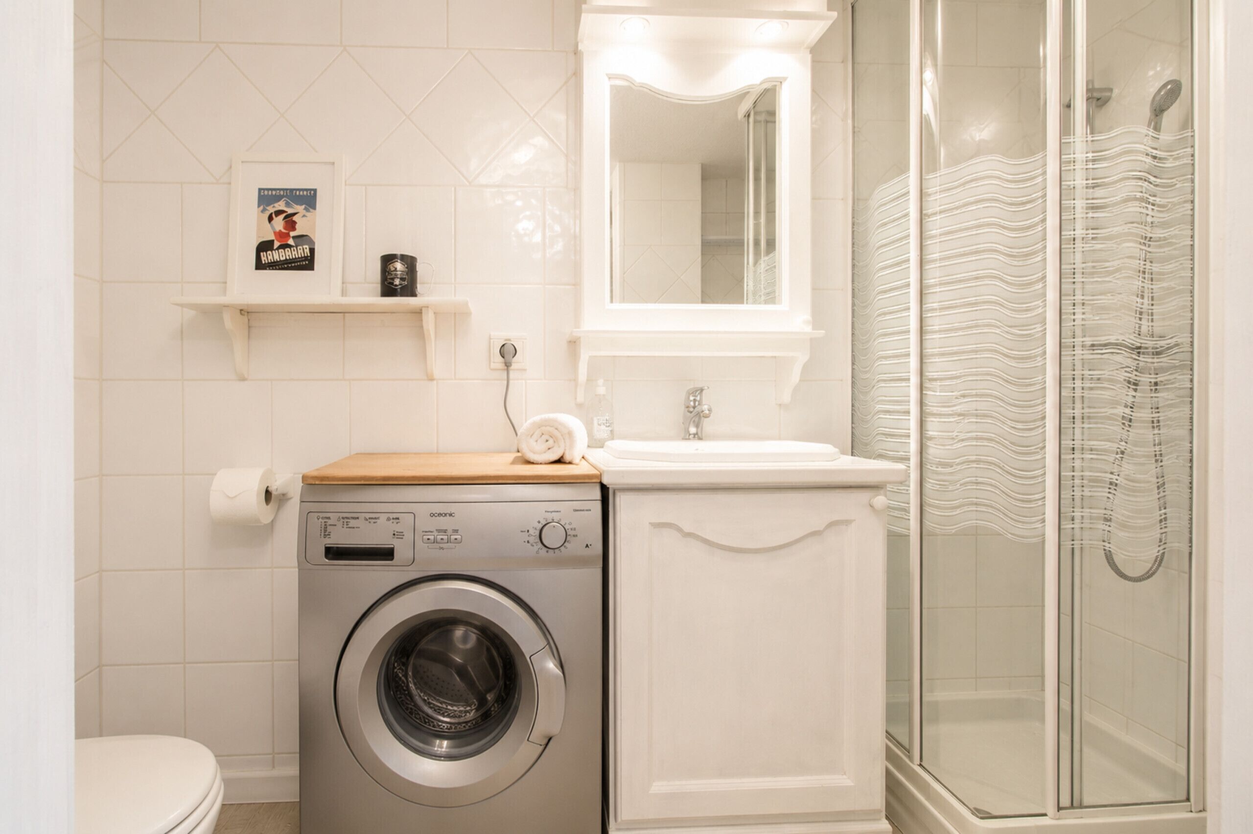 Un baño pequeño con lavadora, lavamanos y cabina de ducha de vidrio.