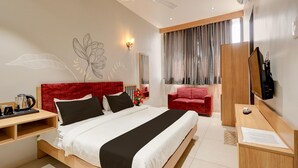 A modern hotel room with a large bed, a desk, a red chair, a TV, and a ceiling fan. - Deluxe Matoshree Palace (Satara)
